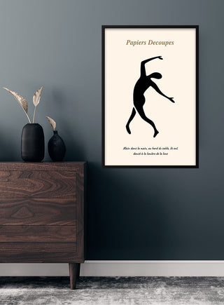Minimalist French art poster of a black dancer silhouette hangs on a dark wall above a wooden dresser with decor.