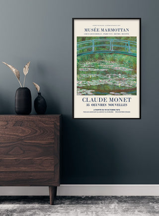 Framed Claude Monet "The Japanese Bridge" poster hanging on a dark wall above a wooden dresser with vases.