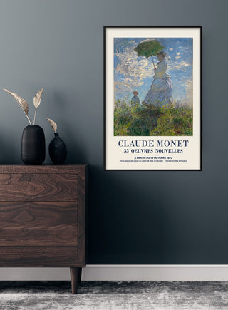 Poster of "Madame Monet og hendes søn" by Claude Monet hanging on a dark wall above a wooden dresser.