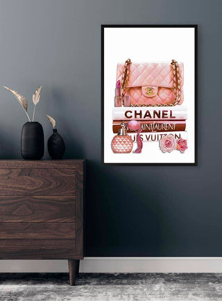 Framed art print featuring a pink handbag, fashion books, and accessories, styled in a modern room.