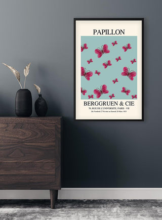 Framed Inspired Papillon No. 05 Plakat featuring pink butterflies on a light blue background above a dresser.