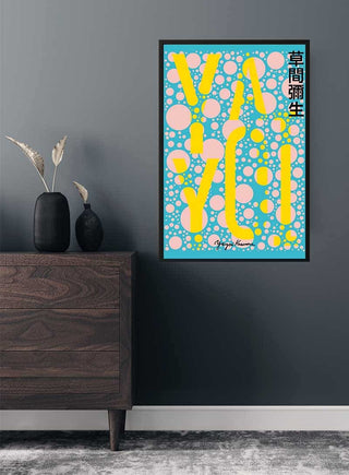 Framed Yayoi Kusama yellow on blue plakat with polka dots, displayed on a dark wall above a wooden cabinet.