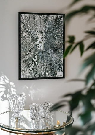 Tiger in the Leaves by JHN.ByHjort in a black frame above a glass table with crystal glassware
