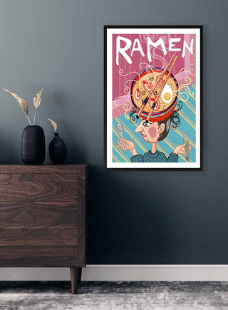 Framed "På Hovedet Ramen" print by Nina Broen displayed on a dark wall above a wooden dresser.