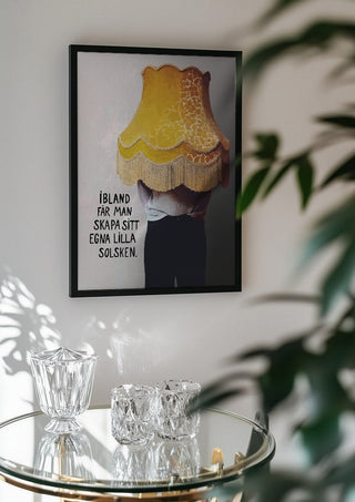 Solsken by Grafik bageri in a black frame above a glass table with crystal glassware