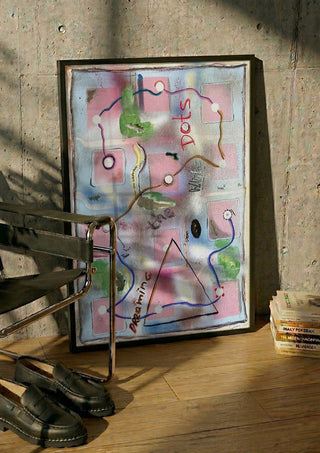 Dreaming The White Dots by Art Guveau in a black frame leaning against a concrete wall by a steel chair