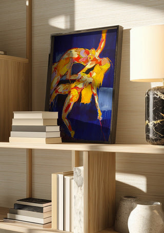 Two Figures in Blue by René J in a dark frame on a wooden shelf beside books and a lamp