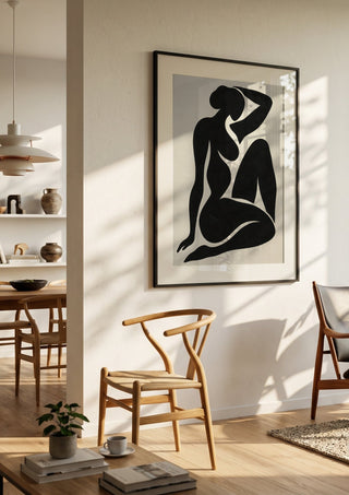 Black Nude Silhouette – Minimalist Abstract Figure Wall Art by TimlessArtworks in a black frame in a bright dining room with wooden chairs