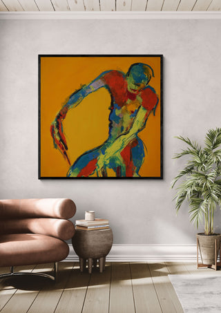 Bending Figure by René J in a black frame above a tan leather chair beside a potted plant
