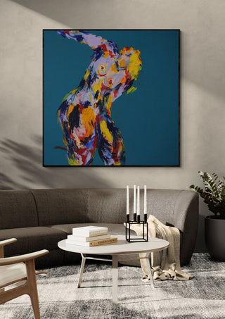 Leaning Back by René J in a black frame above a grey sofa with a round coffee table and candlesticks