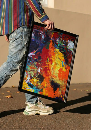 Red Abstract by René J carried in a black frame along a sunny street