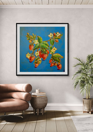 Strawberries on Blue by Svetla Stoyanova Bassi in a black frame above a tan leather chair beside a potted plant