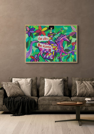 To Do: Be Iconic by Camilla Nilsson in a light wood frame above a grey sofa with cushions