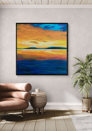 Under An Evening Sky by Finbar Stevens in a black frame on a pale wall beside a leather armchair and a palm