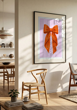Orange velvet bow on pink by Ohkimiko in a black frame in a bright dining room with wooden chairs