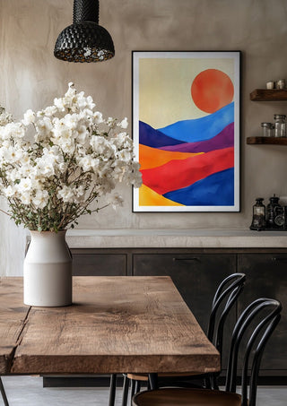 Red sun over colourful hills by Ohkimiko in a black frame above a rustic table with white flowers