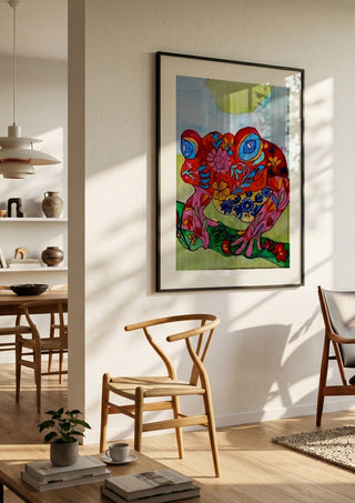Color frog by Nittaart in a black frame in a bright dining room with wooden chairs