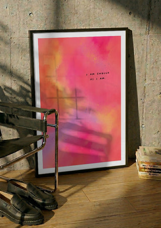 I Am Enough by Decker Studios in a black frame leaning against a concrete wall by a steel chair