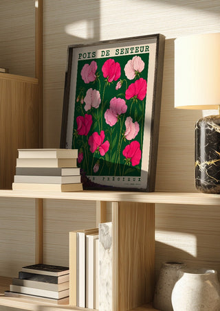 POIS DE SENTEUR by Annika Persson in a dark frame on a wooden shelf beside books and a lamp