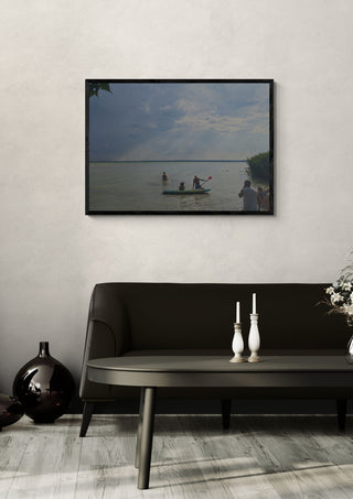 The Lake’s Shared Rhythm by Bora Kőhalmi in a black frame on a pale wall above a dark sofa with candlesticks