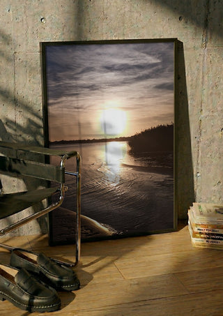 Light Finding the Shore by Bora Kőhalmi in a black frame leaning against a concrete wall by a steel chair
