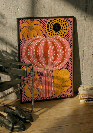 Pink Dotted Pumpkin by Yokohama in a black frame leaning against a concrete wall by a steel chair