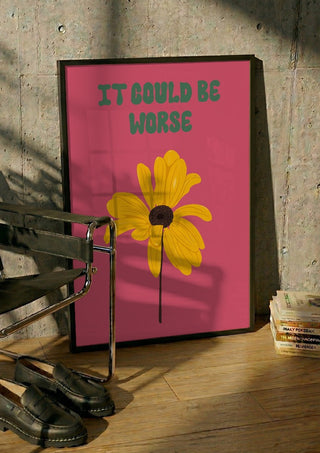 It Could Be Worse by Jakob Falkenberg in a black frame leaning against a concrete wall by a steel chair