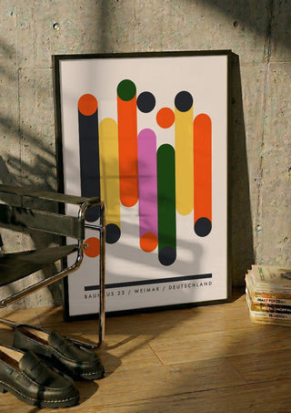 Bauhaus Columns by Neil Stevens in a black frame leaning against a concrete wall by a steel chair