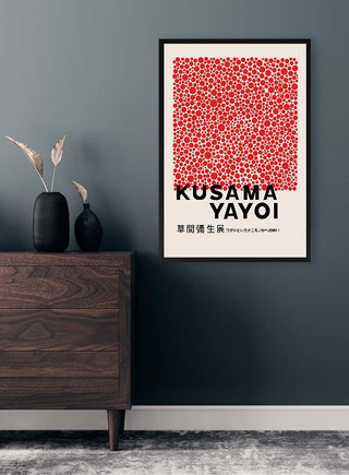 Framed Yayoi Kusama Red Dots Plakat hanging on a dark wall above a wooden dresser with vases.