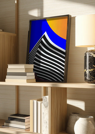 Pyramid by Aleksi Allan in a dark frame on a wooden shelf beside books and a lamp