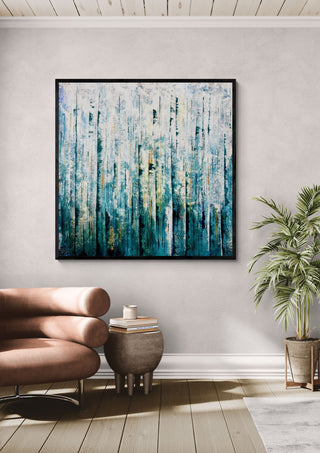 Teal Abstract by Marina Agre in a black frame on a pale wall above a tan leather chair and a potted palm
