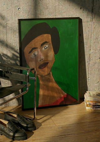 Sinthea by Ian Frederick Harris in a black frame leaning against a concrete wall by a steel chair