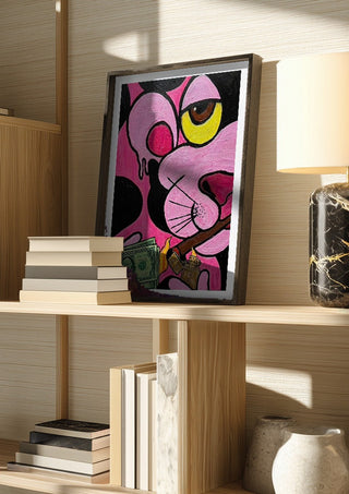 Capitalist Illusion by Bibi in a dark frame on a wooden shelf beside books and a lamp