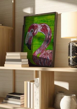 Vibrant Flamingo by Bibi in a dark frame on a wooden shelf beside books and a lamp