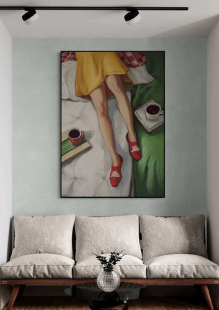 Wall art print of "Coffee Break" by Martina Karlsson above a modern sofa, featuring legs, coffee cups, and books.