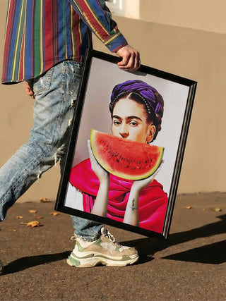 Person holding framed art of Frida Kahlo with a watermelon slice covering her mouth, titled "Watermelon Frida - Dikhotomy."