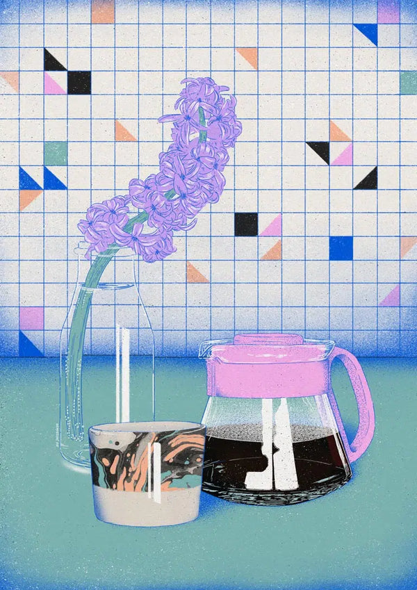 Glass coffee drip pot filled with coffee beside a cup and purple flower, on a tiled background.