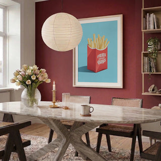A framed Fries Before Guys - Andreas Magnusson print hangs on a red wall above a dining table in a modern room.