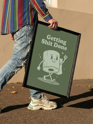 Person holding a framed "Getting Things Done" poster with cartoon toilet paper, product by Andreas Magnusson.