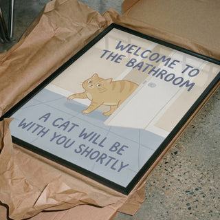 Framed print of a cat by a bathroom door with text: "Welcome to the bathroom, a cat will be with you shortly."