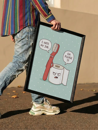 Person holding framed "Grumpy Bathroom Talk" art with cartoon toothbrush and toilet paper by Andreas Magnusson.