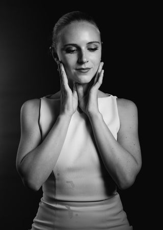 Quiet Light by Bettinafloorphoto - a woman in white against a black ground with hands at her face