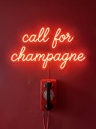 Red neon sign reading "call for champagne" above a vintage red phone, on a product page for Andreas Magnusson.