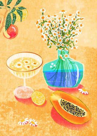 A vase of daisies, a cocktail, papaya, and citrus decorate a table in Summer Day Vibes by Raissa Oltmanns.
