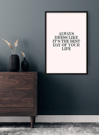 Framed "Always dress like it's the best day of your life" poster on wall above wooden dresser in modern room.
