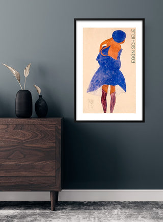 Framed art print of Egon Schiele's "Standing Girl, Back View (1908)" displayed on a dark wall above a wooden dresser.