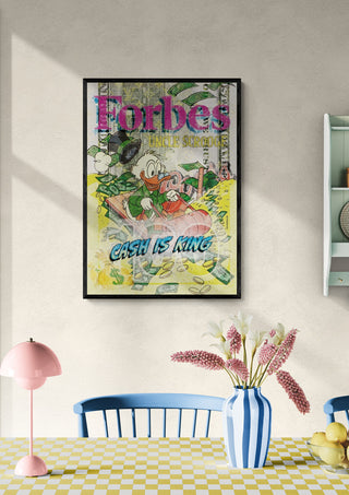 Framed "Cash is King - Ricardo Noble" artwork on a wall above a dining table with flowers and pastel decor.