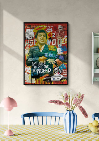 Framed Scarface - Ricardo Noble artwork on a light wall above a dining table with flowers and striped vase.