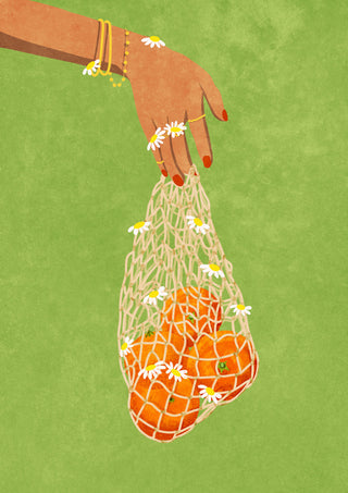 A hand holding a mesh bag filled with fresh oranges decorated with small flowers on a green background.