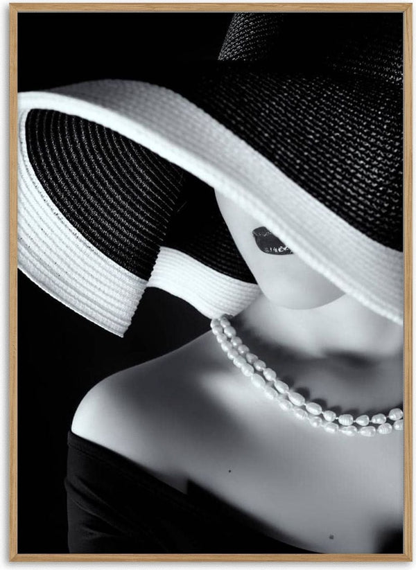Black and white portrait of a woman in a wide-brim hat, pearl necklace, and off-shoulder dress.